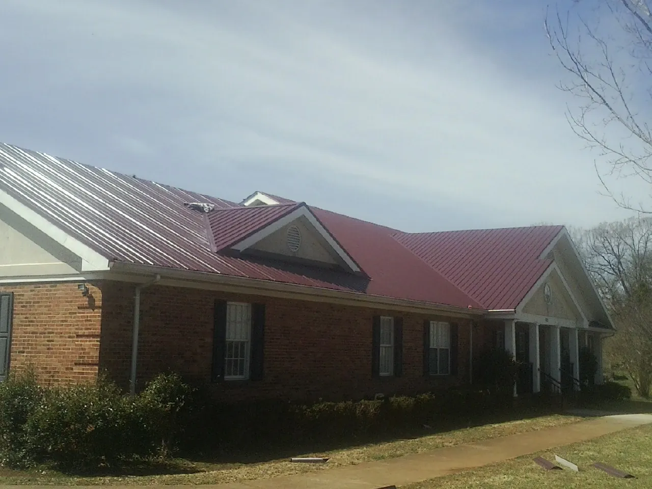 Red metal roof with gabled entries on a long brick building, from a Hail Damage Roof Repair job in Estero