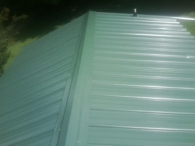 New green metal panels meeting at the ridge of a roof — Flat Roof Repair work by our crew in Estero