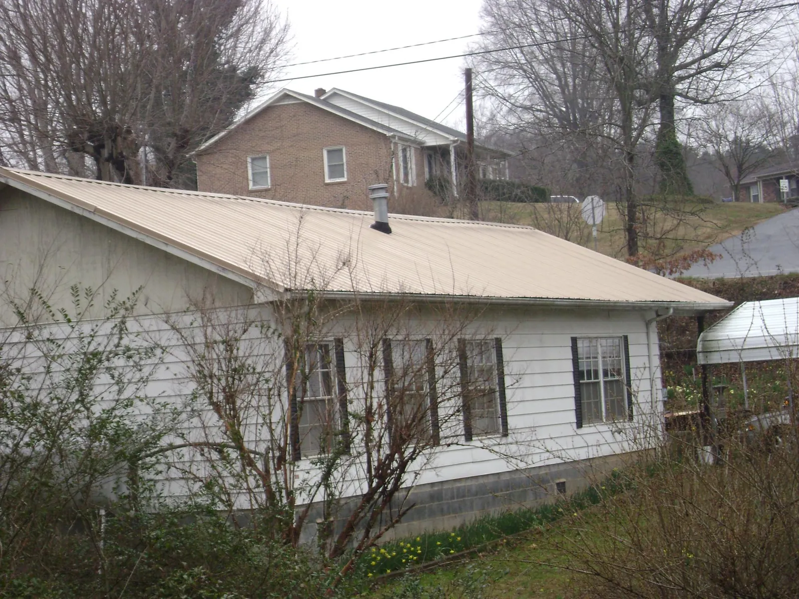 Tan metal roof on a white sided house set into a hillside — Commercial Roofing by Roofing Brothers in Estero